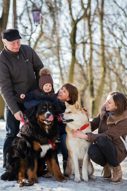 Feliz familia posa con divertido Akita-inu y perro de montaña de Bernese en la nieve