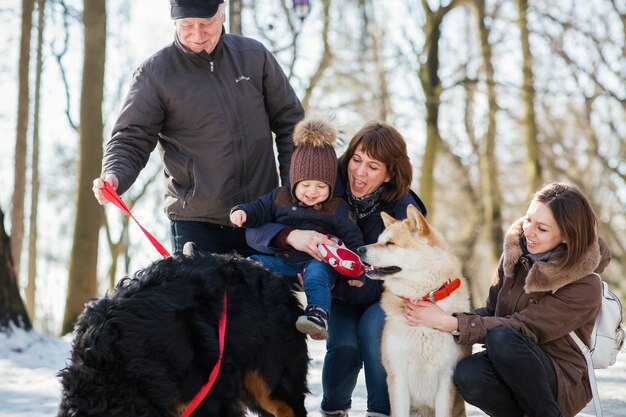 Feliz familia posa con divertido Akita-inu y perro de montaña de Bernese en la nieve