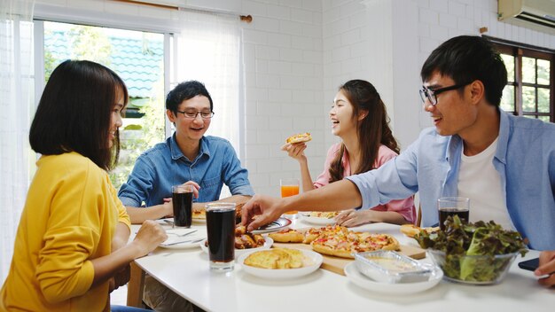 Feliz grupo de jóvenes amigos almorzando en casa. Fiesta familiar de Asia comiendo pizza y riendo disfrutando de la comida mientras están sentados en la mesa de comedor juntos en casa. Fiesta de celebración y unión.