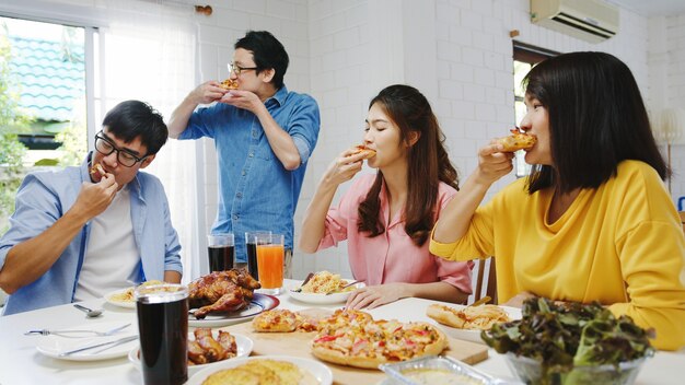 Feliz grupo de jóvenes amigos almorzando en casa. Fiesta familiar de Asia comiendo pizza y riendo disfrutando de la comida mientras están sentados en la mesa de comedor juntos en casa. Fiesta de celebración y unión.