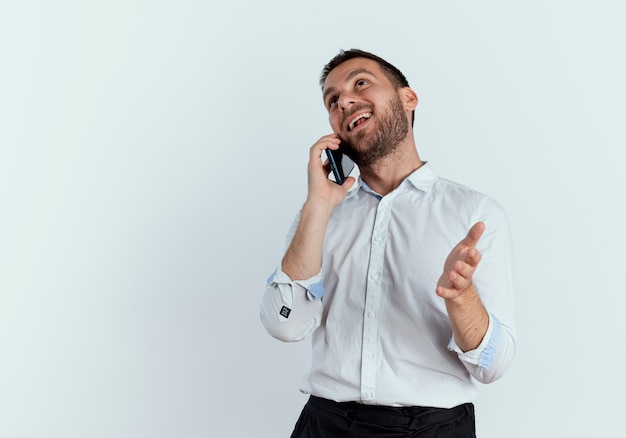 Feliz guapo habla por teléfono mirando hacia arriba aislado en la pared blanca