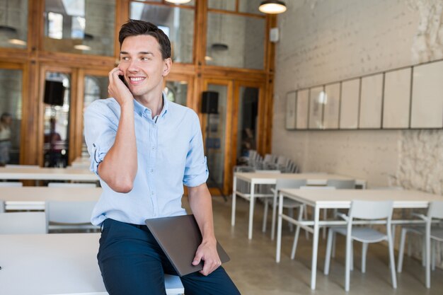 Feliz hablando por teléfono joven atractivo sonriente hombre sentado en la oficina abierta de trabajo conjunto,