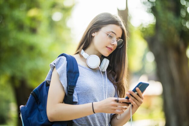 Feliz hermosa joven caucásica con teléfono inteligente verde al aire libre en un día soleado de verano enviando mensajes de texto y sonriendo.
