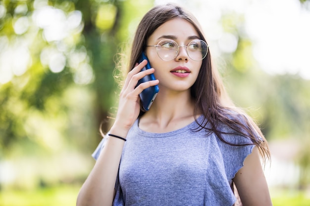 Feliz hermosa joven de pie y hablando por teléfono celular en la ciudad