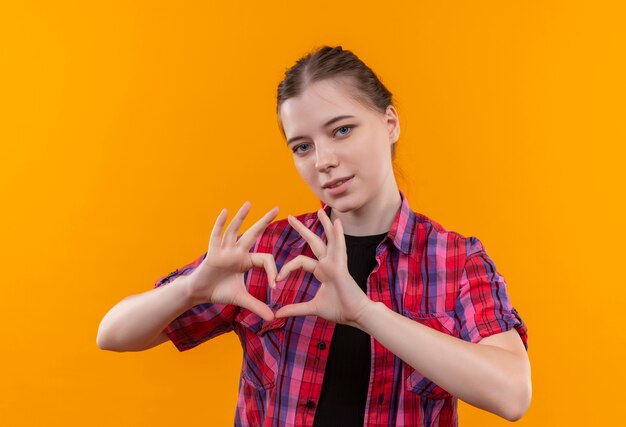 Feliz hermosa joven vestida con camisa roja mostrando gesto de corazón sobre fondo amarillo aislado