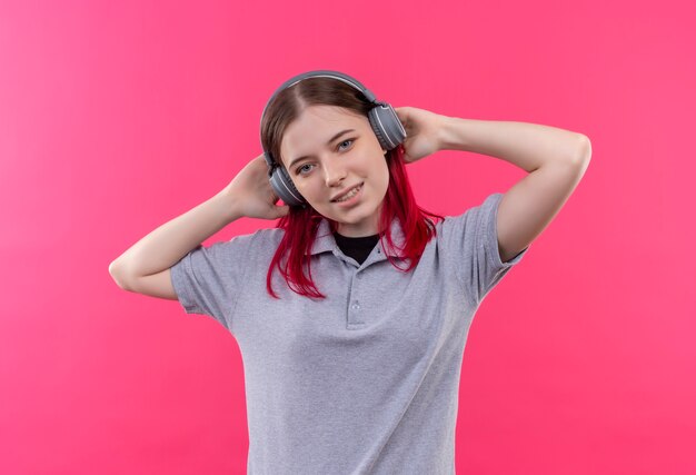 Feliz hermosa joven vestida con camiseta gris escuchar música en auriculares sobre fondo rosa aislado