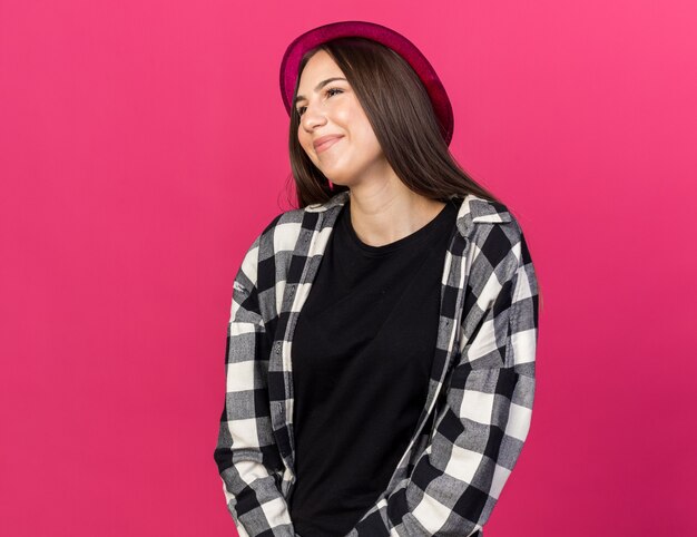 Feliz hermosa joven vistiendo gorro de fiesta aislado en la pared rosa