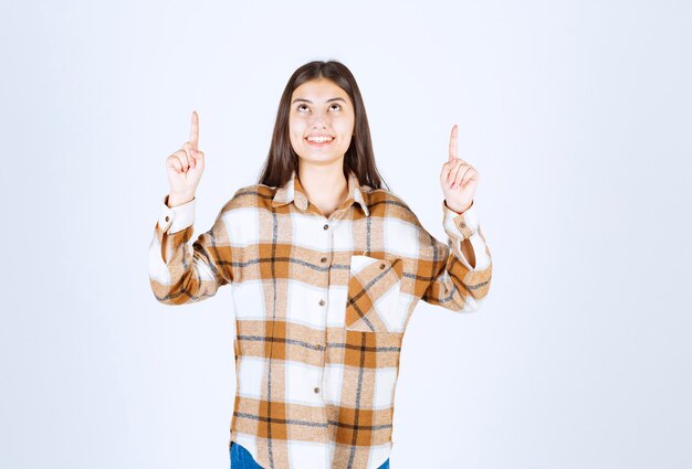 Foto gratuita feliz hermosa mujer apuntando a algún lugar de la pared blanca.