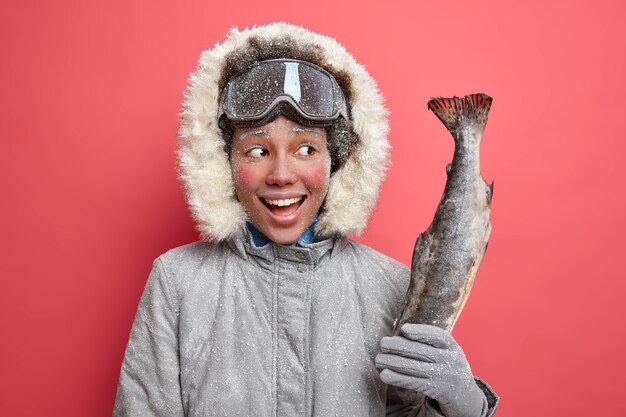 Feliz hermosa mujer cubierta con escarcha en invierno y yendo a pescar pasa el tiempo libre al aire libre vestida con ropa de abrigo durante el frío día helado.