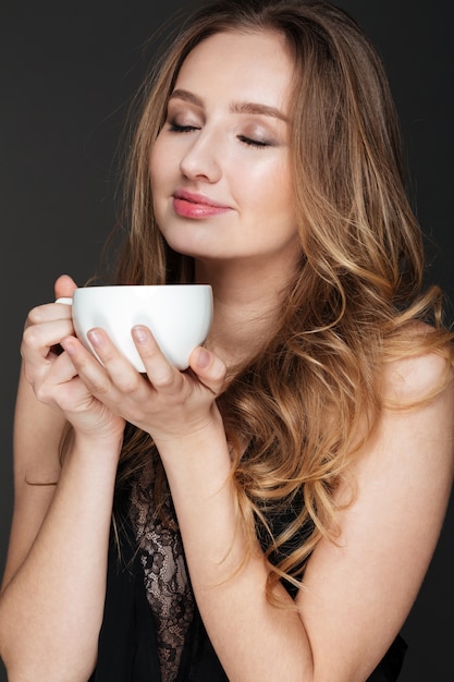 Feliz hermosa mujer joven de pie y sosteniendo la taza de café