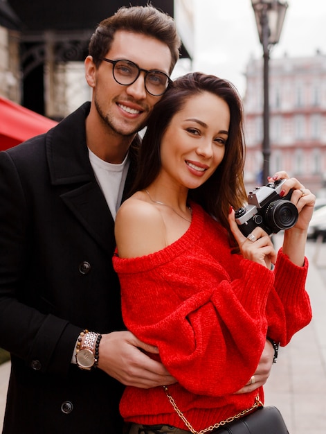 Feliz hermosa pareja vergonzosa y posando en la calle de vacaciones. Estado de ánimo romántico. Mujer morena con cámara de película.