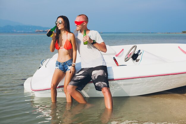 Feliz hipster mujer y hombre bebiendo cerveza en vacaciones tropicales de verano en Tailandia viajando en barco en el mar, fiesta en la playa, gente divirtiéndose juntos, emociones positivas