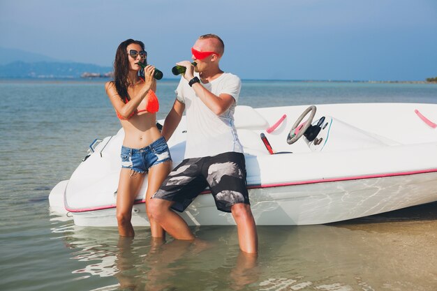Feliz hipster mujer y hombre bebiendo cerveza en vacaciones tropicales de verano en Tailandia viajando en barco en el mar, fiesta en la playa, gente divirtiéndose juntos, emociones positivas