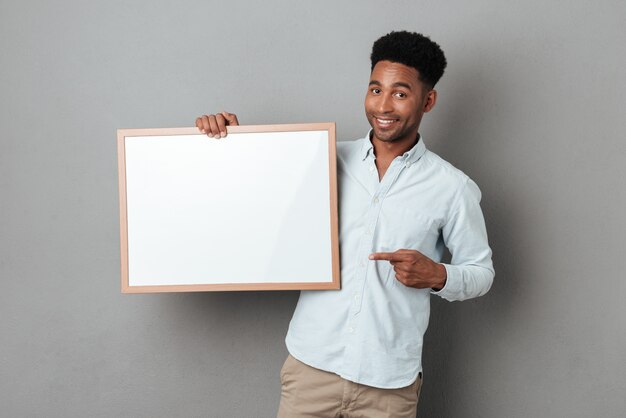 Feliz hombre africano sonriente dedo acusador en el tablero en blanco