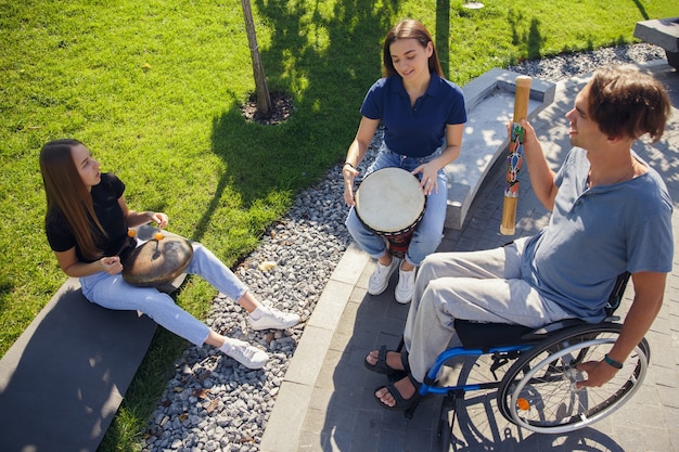 Feliz hombre discapacitado en silla de ruedas pasar tiempo con amigos tocando música instrumental en vivo al aire libre.