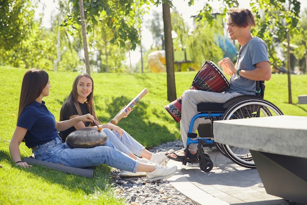 Feliz hombre discapacitado en silla de ruedas pasar tiempo con amigos tocando música instrumental en vivo al aire libre.