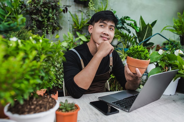 Feliz el hombre jardinero usa un teléfono inteligente y una computadora portátil mientras ofrece un tutorial en línea sobre planes en macetas en la tienda