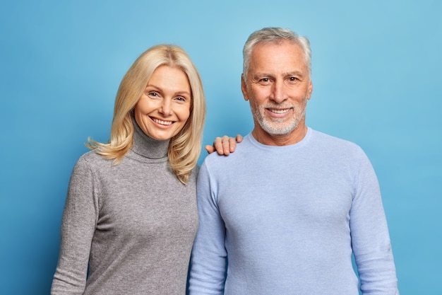 Feliz el hombre y la mujer senior expresan emociones positivas plantean juntos estando todavía enamorados aislados sobre la pared azul