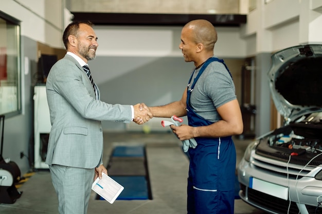 Feliz hombre de negocios y apretón de manos mecánico afroamericano en el taller de reparación de automóviles