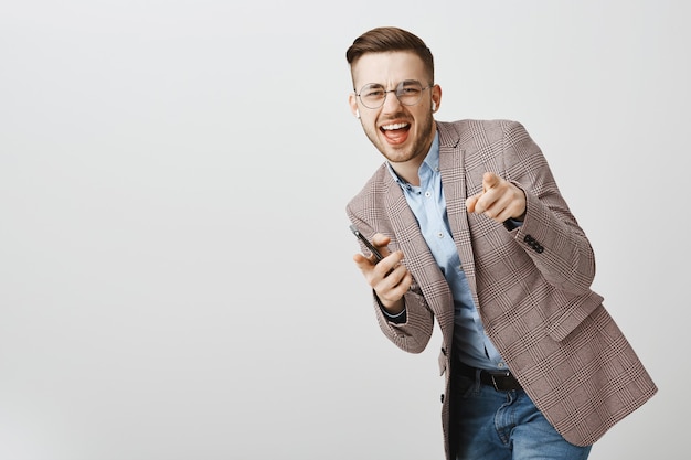 Feliz hombre de negocios bailando en regocijo con el teléfono inteligente, escuchando música en auriculares inalámbricos