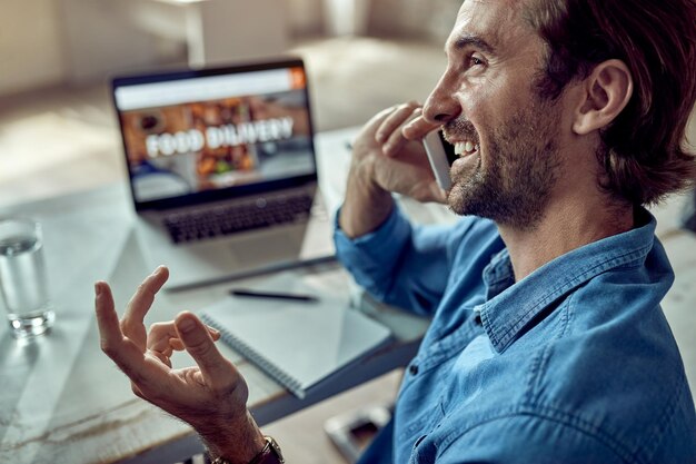 Feliz hombre de negocios comunicándose por teléfono celular mientras trabaja en la oficina