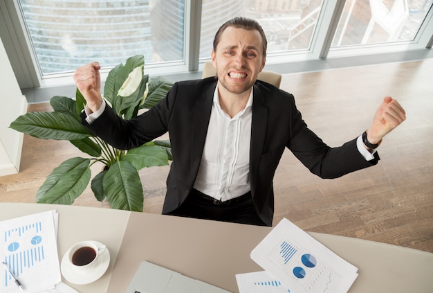 Foto gratuita feliz hombre de negocios en el escritorio celebrando logros