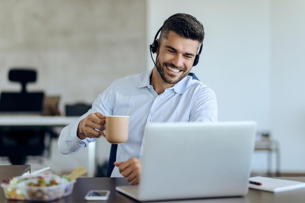 Feliz hombre de negocios haciendo videollamadas mientras toma un café en la oficina