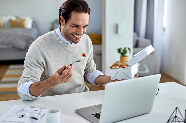 Feliz hombre de negocios navegando por la red en una laptop durante su almuerzo en casa