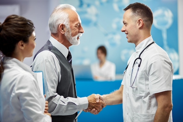 Foto gratuita feliz hombre de negocios senior y médico dándose la mano mientras saluda en un pasillo del hospital