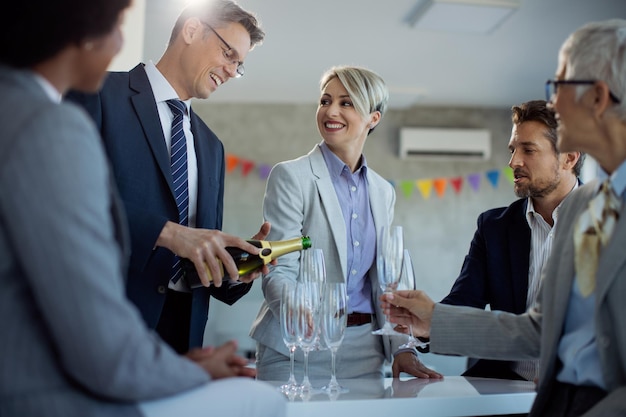 Feliz hombre de negocios sirviendo champán mientras celebra con colegas en la oficina