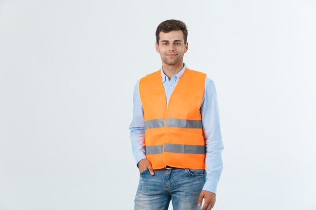 Feliz ingeniero sonriendo y de pie con confianza, chico vestido con camisa caro y jeans con chaleco naranja, aislado sobre fondo blanco.