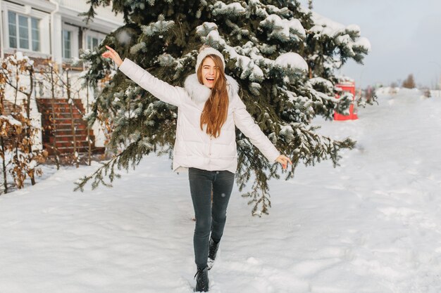 Feliz invierno helado en mañana soleada en la calle de una mujer bonita alegre divirtiéndose en la nieve.