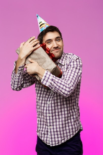 Feliz joven abrazando regalo de cumpleaños en caja sobre pared púrpura.