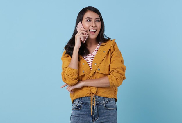 Feliz joven adolescente asiática mujer hablando de teléfono móvil aislado sobre fondo azul studio