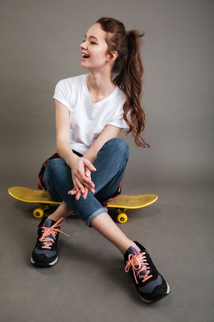 Foto gratuita feliz joven adolescente sentado en patineta y riendo