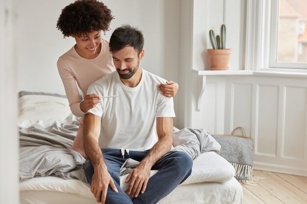 Feliz joven afroamericana muestra prueba de embarazo positiva a su marido