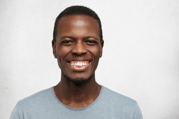 Feliz joven afroamericano sonriendo alegremente mostrando sus dientes blancos rectos perfectos, posando aislado