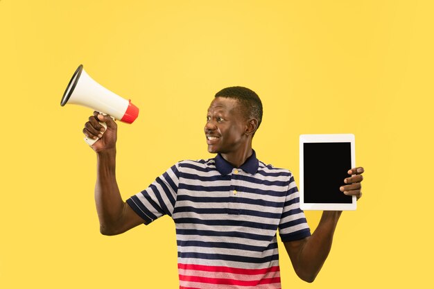 Feliz joven afroamericano con tableta aislado sobre fondo amarillo studio