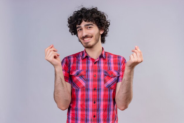 Un feliz joven apuesto con el pelo rizado en camisa a cuadros mostrando gesto de dinero