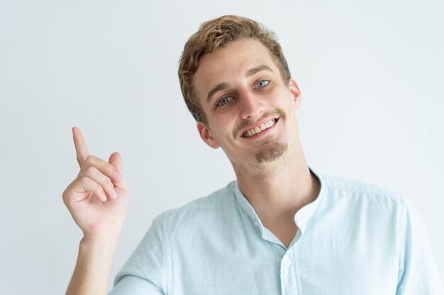 Feliz joven apuntando el dedo hacia arriba. Chico guapo que recomienda algo.