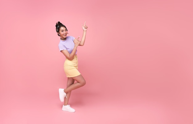 Feliz joven asiática adolescente mujer de pie con su dedo apuntando aislado sobre fondo de color rosa