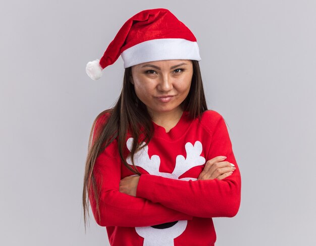 Feliz joven asiática vistiendo gorro de navidad con suéter cruzando las manos aisladas sobre fondo blanco.