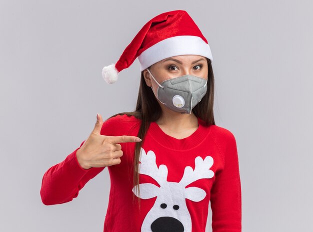 Feliz joven asiática vistiendo gorro de navidad con suéter y puntos de máscara médica en el lado aislado sobre fondo blanco con espacio de copia
