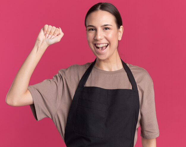 Feliz joven barbero morena en uniforme se encuentra con el puño levantado