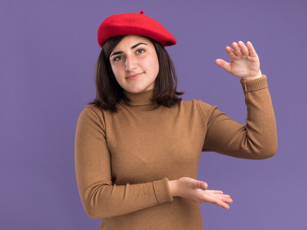 Feliz joven bastante caucásica con sombrero de boina fingiendo sostener algo