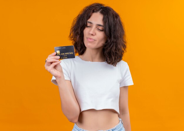 Feliz joven bella mujer sosteniendo la tarjeta y mirándola en la pared naranja aislada con espacio de copia