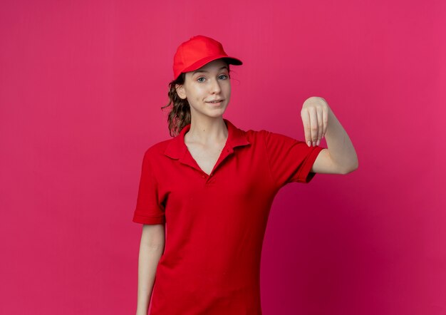 Feliz joven bonita repartidora en uniforme rojo y gorra finge sostener algo