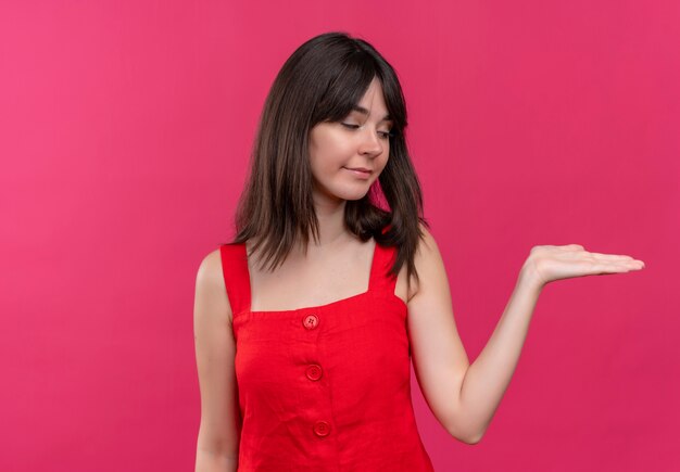 Feliz joven caucásica mira su mano vacía sobre fondo rosa aislado