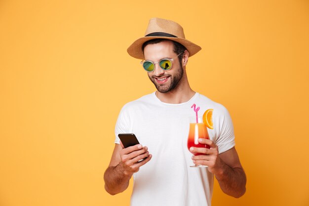 Feliz joven chateando por teléfono móvil con cóctel.