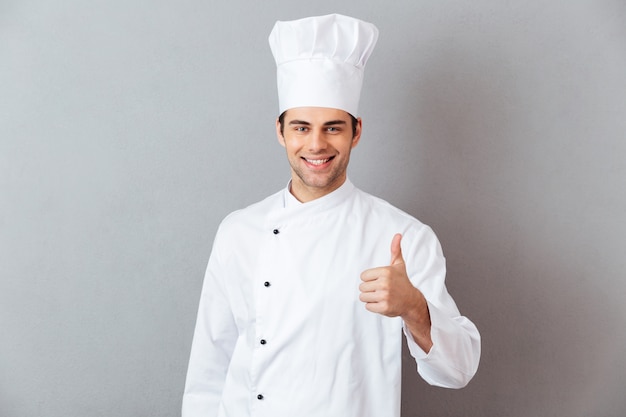 Feliz joven cocinero en uniforme mostrando los pulgares para arriba.